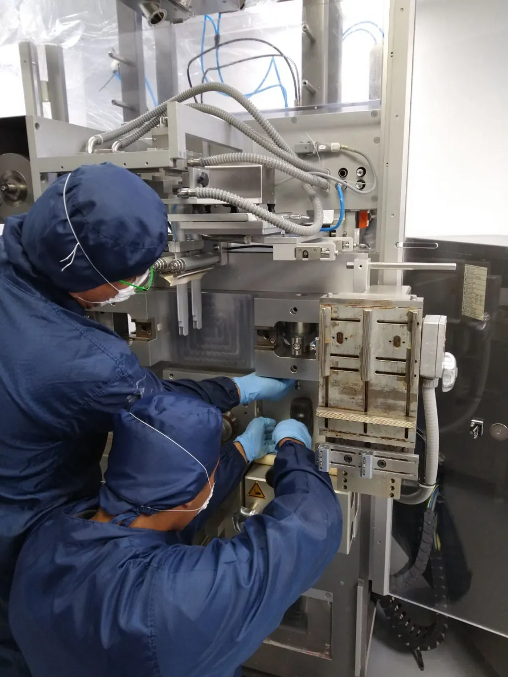 Técnico con equipo de protección trabajando en una máquina de la industria farmacéutica